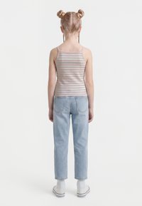 Child with blonde hair in two buns and braids, wearing a pink striped tank top, light blue jeans, white socks, and white sneakers, facing away.