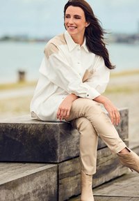 Losse witte blouse met beige accenten, beige aansluitende broek en beige enkelboots; gladde textuur met een knoopsluiting.