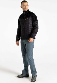 Schwarze isolierte Jacke mit gepuffter Textur, orangefarbenen Akzenten und hohem Kragen; kombiniert mit grauen Hosen und schwarzen robusten Schuhen.