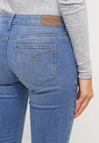 Blå denimjeans med medelhög midja, med en läderlogotyp på baksidan, dekorerad sömnad och standard bakfickor.