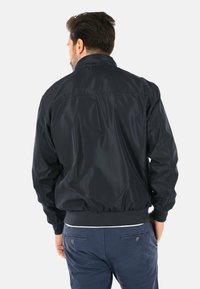 Giacca bomber navy con una finitura liscia e lucida, maniche a costine e colletto alto. Presenta una vestibilità comoda e una vita elastica.
