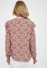 Bluzka z długim rękawem z lekkiego materiału, zdobiona kwiatowym wzorem w odcieniach różu i brązu. Fala na szwach ramion.