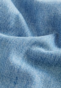 Denimstof in lichtblauw met een zachte textuur, met een subtiel geweven patroon. Het materiaal lijkt glad met zachte kreukels.