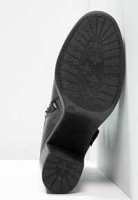 Zapato de cuero negro con suela de goma texturizada, que presenta un tacón bajo y costuras detalladas. La suela tiene un diseño con patrón para mayor tracción.