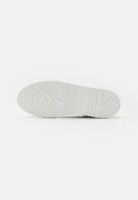 Semelle de chaussure blanche avec un motif de grip texturé, présentant des rainures et des crêtes pour une meilleure traction. Conçue pour la durabilité et la stabilité.