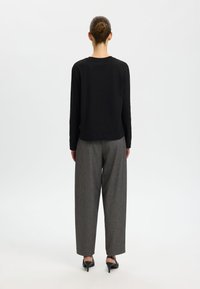 Black long-sleeve top paired with high-waisted gray plaid trousers and black open-toe heels, viewed from the back. Simple, clean design.