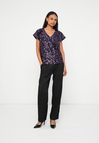 Lilla top med palietter, V-hals og korte ærmer, kombineret med sorte, skræddersyede bukser og spidse sorte hæle. Glat tekstur og skinnende pynt.