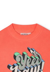 Felpa color corallo con colletto a costine, caratterizzata da un audace design grafico multicolore con il testo "Yee-haw!" e un'illustrazione di una mano giocosa.