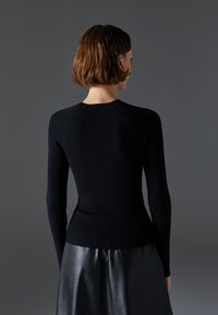 Black ribbed sweater featuring long sleeves and a fitted design, paired with a black leather skirt, presented against a neutral background.
