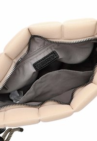 Borsa a mano beige con un esterno strutturato e imbottito. L'interno presenta una foderatura grigia e un compartimento con zip dotato di un'etichetta nera.