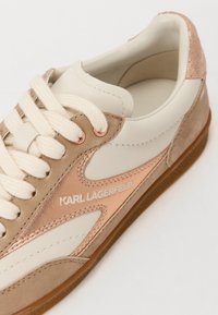 Baskets Karl Lagerfeld crème, beige et or rose avec lacets blancs et semelle en caoutchouc marron, vues en angle montrant les détails latéraux et supérieurs.