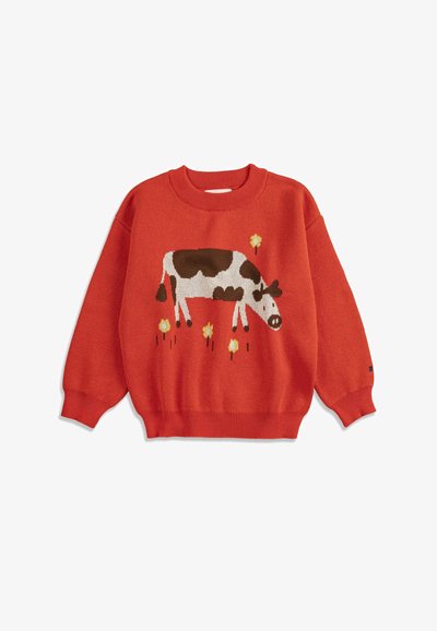 Pull en tricot rouge avec un motif de vache marron et blanc et de fleurs jaunes sur le devant, avec des poignets et un ourlet côtelés.