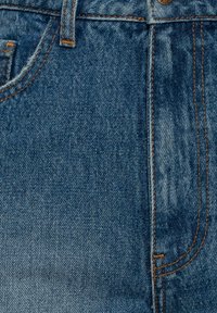 Tejido de mezclilla azul con detalles de costura visibles. Presenta una textura suave y un diseño de cintura alta con bolsillos.