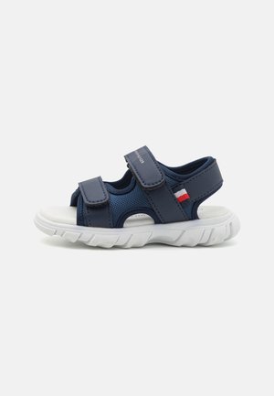 Marineblå åben tå sandal med justerbare velcro stropper og hvid tyk polstret sål, med et lille rødt, hvidt og blåt stofmærke.
