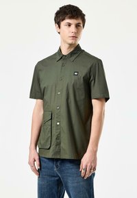 Korte mouw olijfgroene shirt met een puntkraag, voor knopen, een patch zak en een klein logo op de borst.