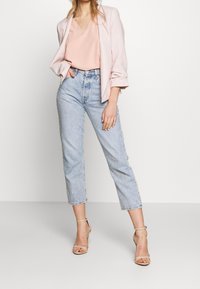 Haut à col en V couleur blush associé à un blazer rose pâle, jean taille haute bleu clair et sandales à lani ères couleur nude. Tenue décontractée mais soignée.