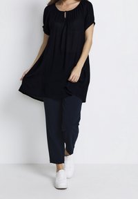 Túnica negra de manga corta, escote con abertura en forma de llave y ajuste relajado, combinada con pantalones azul marino y zapatillas blancas. Textura de tela suave.