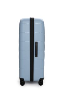 Valigia rigida di colore azzurro chiaro, con superficie testurizzata, cerniere nere, maniglia laterale e quattro ruote nere per la mobilità.