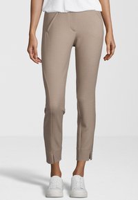 Pantalon beige à motifs avec une coupe ajustée, doté de poches latérales, de fentes aux chevilles et d'une texture lisse, associé à des baskets blanches.