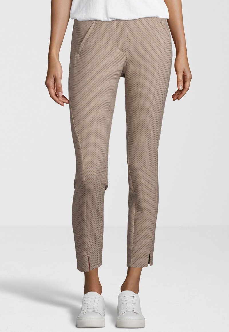 Pantalon beige à motifs avec une coupe ajustée, doté de poches latérales, de fentes aux chevilles et d'une texture lisse, associé à des baskets blanches.