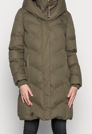 Femme portant un manteau d'hiver matelassé à capuche de couleur vert olive avec fermeture éclair à l'avant et poches, debout devant un fond uni.