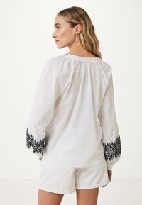 Top bianco a maniche lunghe con accenti neri ricamati sui polsini, caratterizzato da un collo arricciato e una vestibilità rilassata. Abbinato a pantaloni corti bianchi.