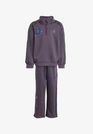 Donkerpaarse Adidas trainingspak met rits aan de voorkant, zwarte strepen op mouwen en broek, en kleine gepixeleerde roze en blauwe bloemdetails.