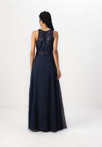 Mörkblå kvällsklänning med spetsbodice, paljettaccent och en flytande kjol. Baksidan har en dragkedja och en scalloperad spetskant.