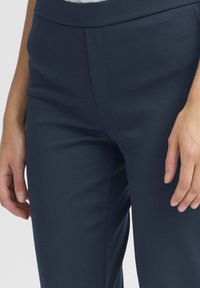 Sima anyagból készült tengerészkék, testhezálló szabású nadrág, lapos elülső résszel és tiszta varrási részletekkel.