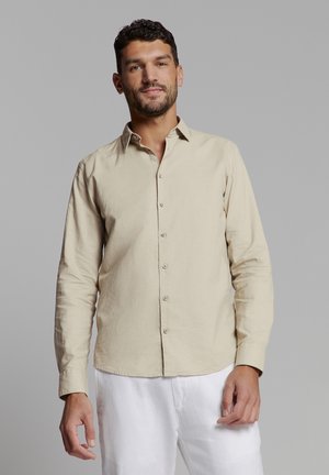 Beige long-sleeve shirt in lightweight fabric with a faded texture, featuring a button-down front and a pointed collar.