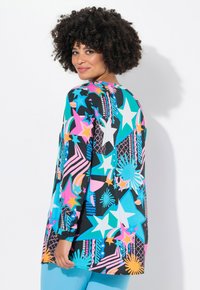Maglietta a maniche lunghe con sfondo nero, caratterizzata da motivi colorati di stelle e geometrie in blu, rosa, arancione e bianco. Tessuto morbido.