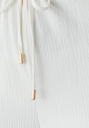 Hvid tekstureret stof med et ribbet mønster, udstyret med snoretræk med guldfarvede cylindriske ender til justering.