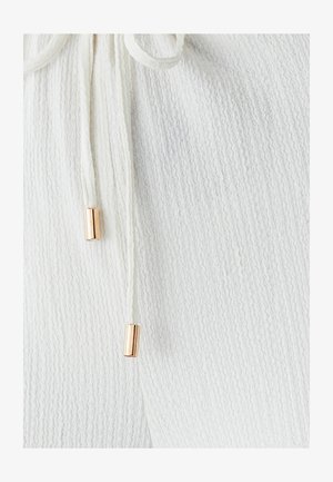 White textured fabric with a ribbed pattern, featuring drawstrings with gold-tone cylindrical ends for adjustment.