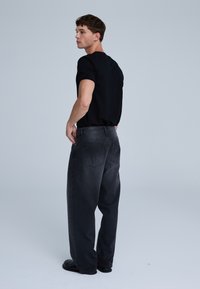 Maglietta nera e jeans in denim grigi. I jeans hanno una vestibilità ampia, tasche posteriori e una finitura scolorita. Completa il look con scarpe nere.