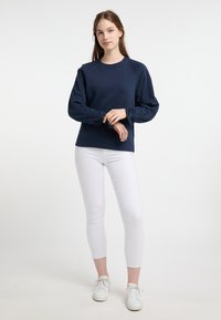 Felpa blu navy con maniche raglan e polsini arricciati, abbinata a leggings bianchi e scarpe da ginnastica bianche. Texture liscia, design casual.