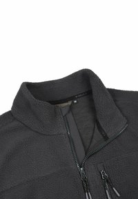 Giacca in pile di colore grigio scuro, con collo alto, zip frontale e due tasche con cerniera, con una finitura morbida e testurizzata. Etichetta della taglia visibile.