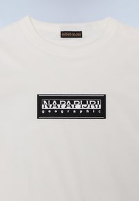 Kreminės spalvos marškinėliai, pagaminti iš medvilnės, su juodu stačiakampiu logotipu, kuriame baltais paryškintais rašmenimis užrašyta "NAPAPIJRI geographic".