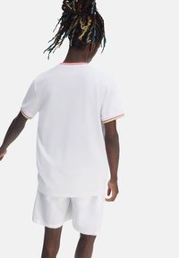 Camiseta blanca de manga corta con acentos de canalé coloridos en las mangas, combinada con pantalones cortos blancos a juego, con un ajuste relajado.
