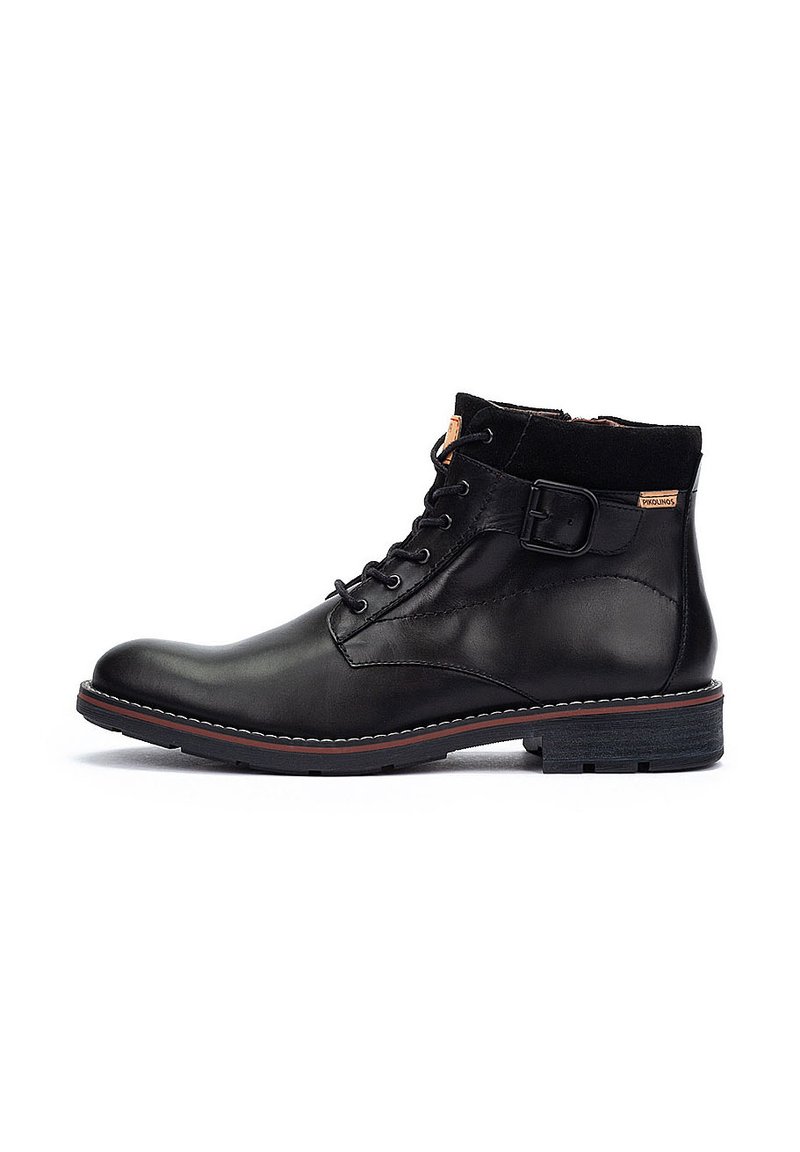 Botín negro de cuero hasta el tobillo con diseño de cordones, acento de hebilla y suela de goma. Textura suave con detalle de costura roja en contraste.