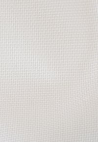 Tessuto bianco testurizzato con un motivo geometrico intrecciato, caratterizzato da una superficie morbida e liscia. Visibili delle piccole linee zigzag rialzate su tutta la superficie.