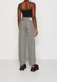 Top corto negro combinado con pantalones de pierna ancha de cintura alta que presentan un patrón floral blanco y una etiqueta sutil en la cinturilla. Zapatos negros gruesos.