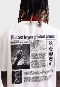 Weißes Baumwoll-T-Shirt mit schwarzen Druckgrafiken, einschließlich Text und Bildern einer Hand und einer Person, sowie einem roten Bandana-Akzent um den Hals.