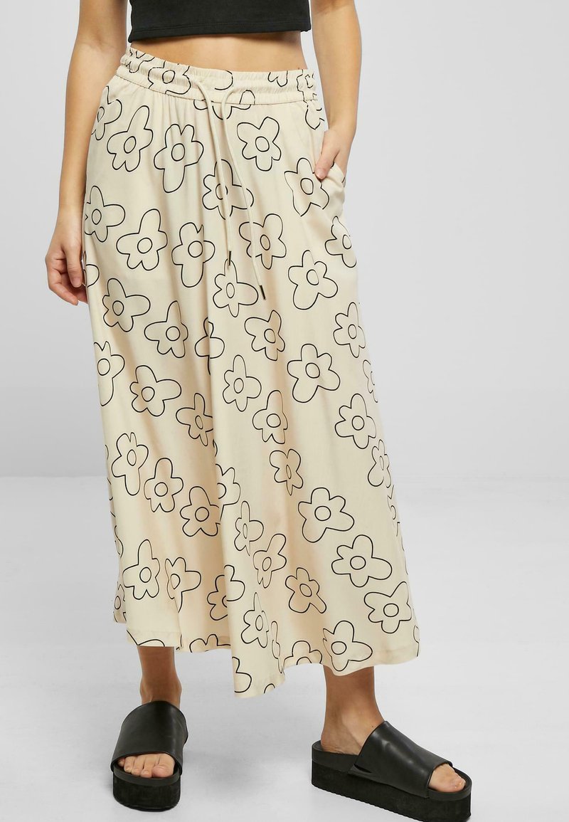 Pantaloni largi, bej deschis, cu talie ajustabilă, având un model floral negru. Asortați cu sandale cu platformă negre.