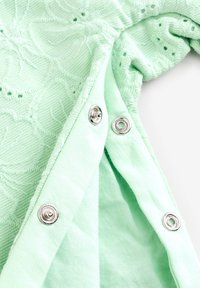 Mintgroene kleding met textuurstof die geborduurde patronen vertoont. Drukknopen zichtbaar langs de rand, aangevuld met een soepele voering.