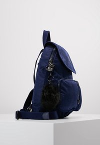 Sac à dos bleu marine avec texture en tissu, rabat supérieur, poche avant et un porte-clés en fausse fourrure. Dispose de bretelles réglables et de fermetures éclair.