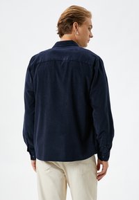 Camisa de pana azul marino con mangas largas, puños de botón y un yugo trasero. Textura suave, ajuste ligeramente relajado y dobladillo curvado.