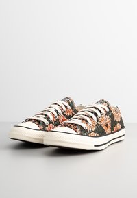 Baskets en toile avec un motif floral orange et vert, arborant des lacets blancs, une bande noire sur la semelle en caoutchouc et un capuchon de orteil texturé.