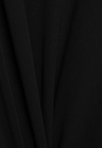 Gros plan sur un tissu noir avec une texture visible et des plis doux créant des lignes verticales et des ombres subtiles.