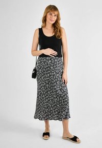 Débardeur noir associé à une jupe midi noire et blanche à motifs floraux, dotée d'un design fluide et d'un tissu léger. Accessoirisé avec un petit sac à main.