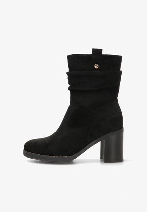 Botín de ante negro con una parte superior caída, punta redonda y tacón grueso. Presenta un pequeño botón dorado como acento y detalles de costura.